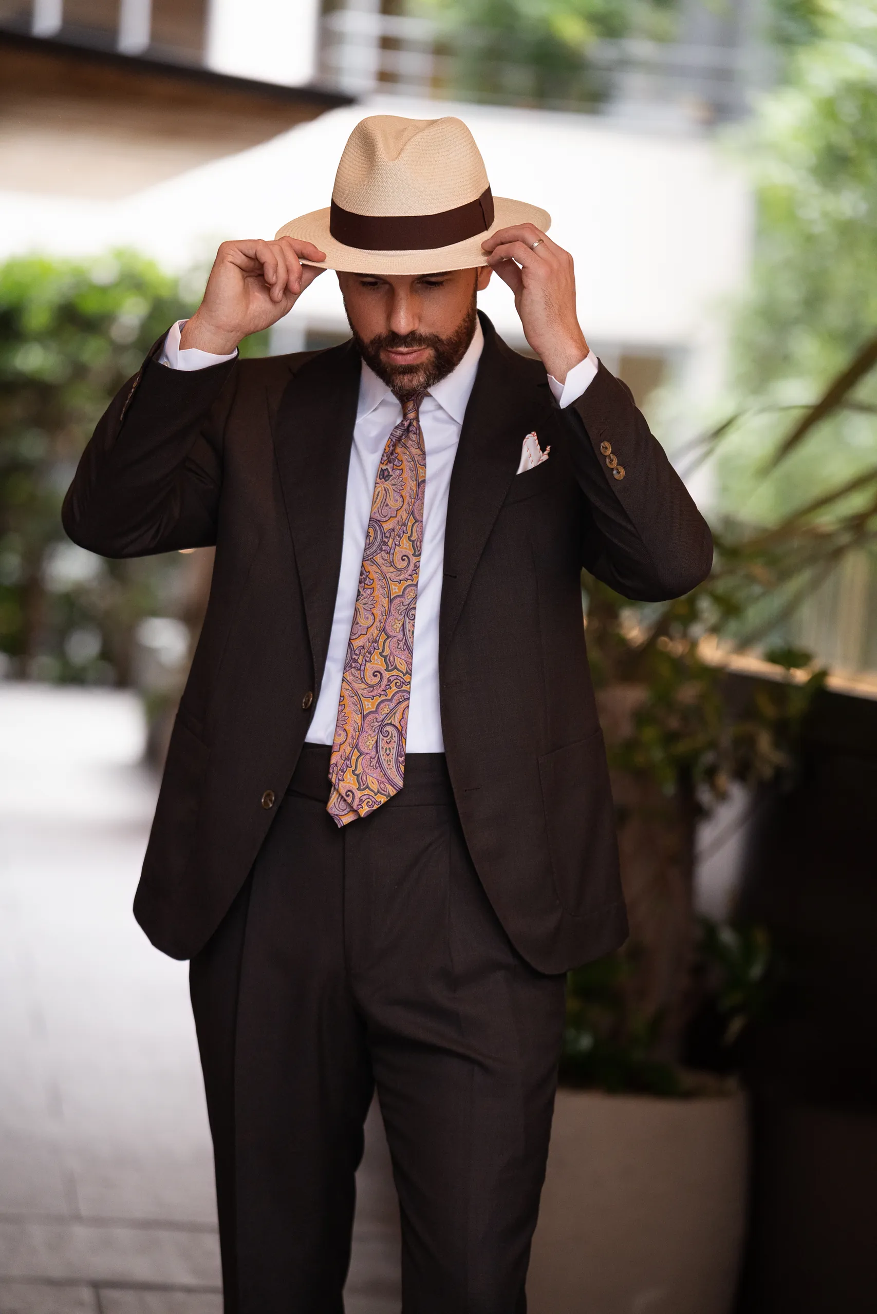 Homme en costume sur mesure brun ajustant son chapeau panama