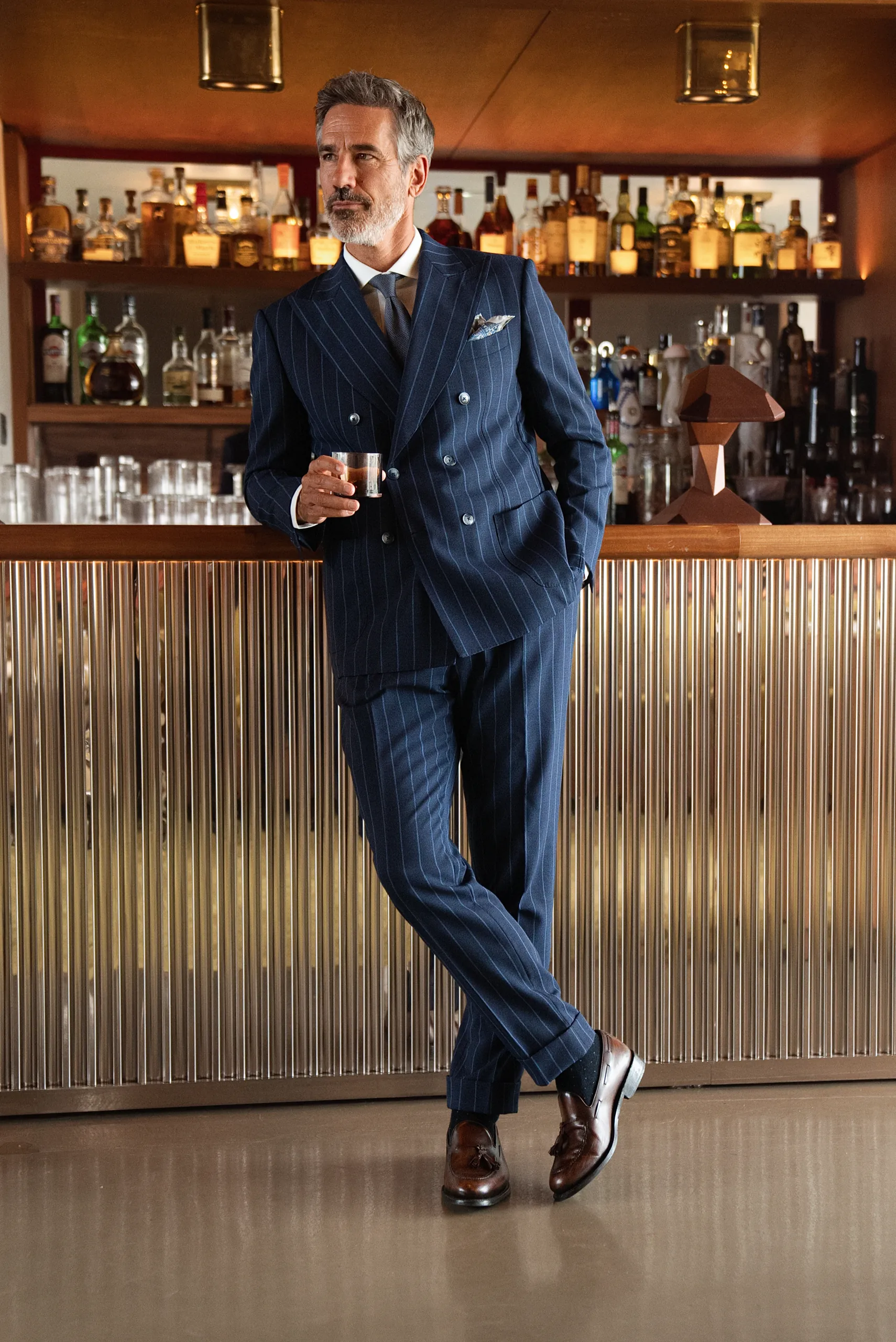 Costume croisé sur mesure bleu marine à rayures, appuyé au comptoir