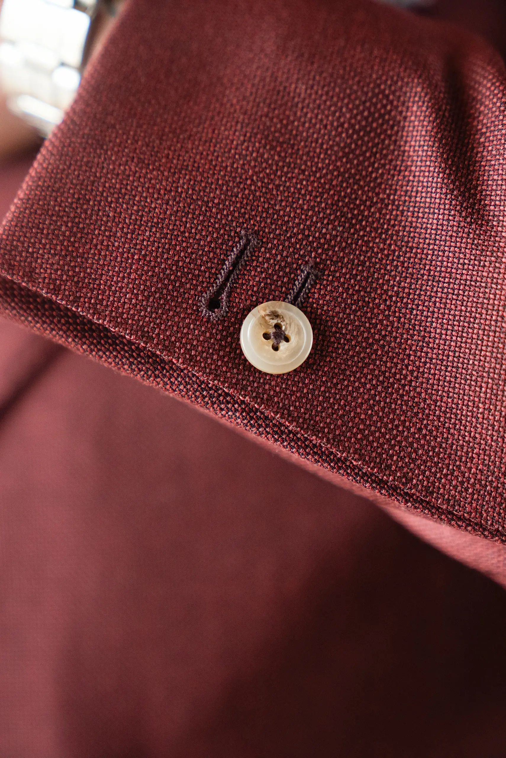 Détail de la boutonnière de revers et du bouton de nacre d'une veste bordeaux