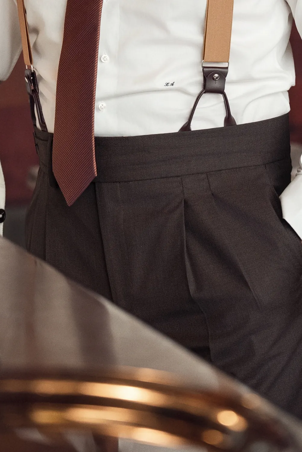 Pantalon sur mesure taille haute brun à pinces, porté avec des bretelles