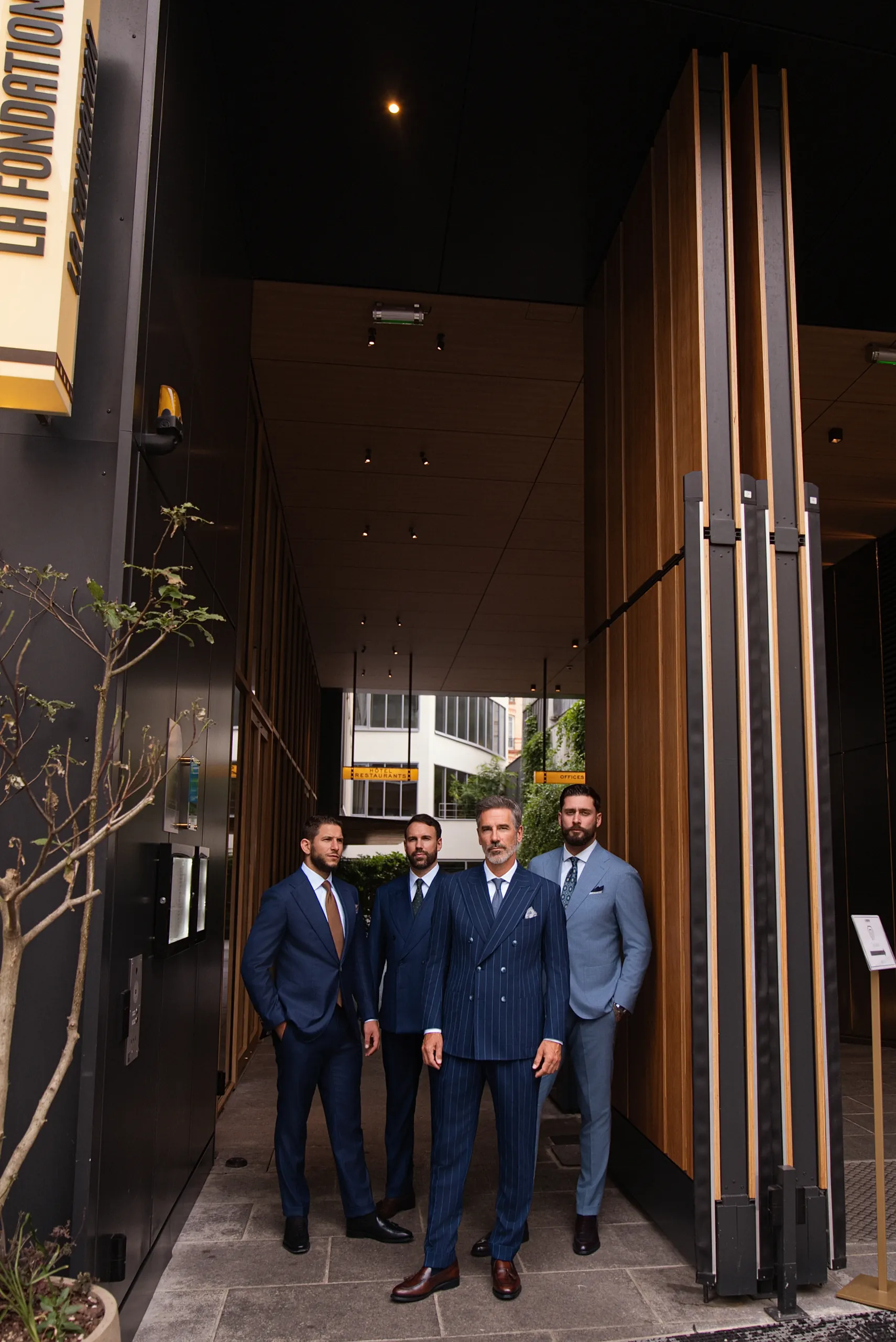 Quatre hommes en costume sur mesure devant l'entrée de La Fondation