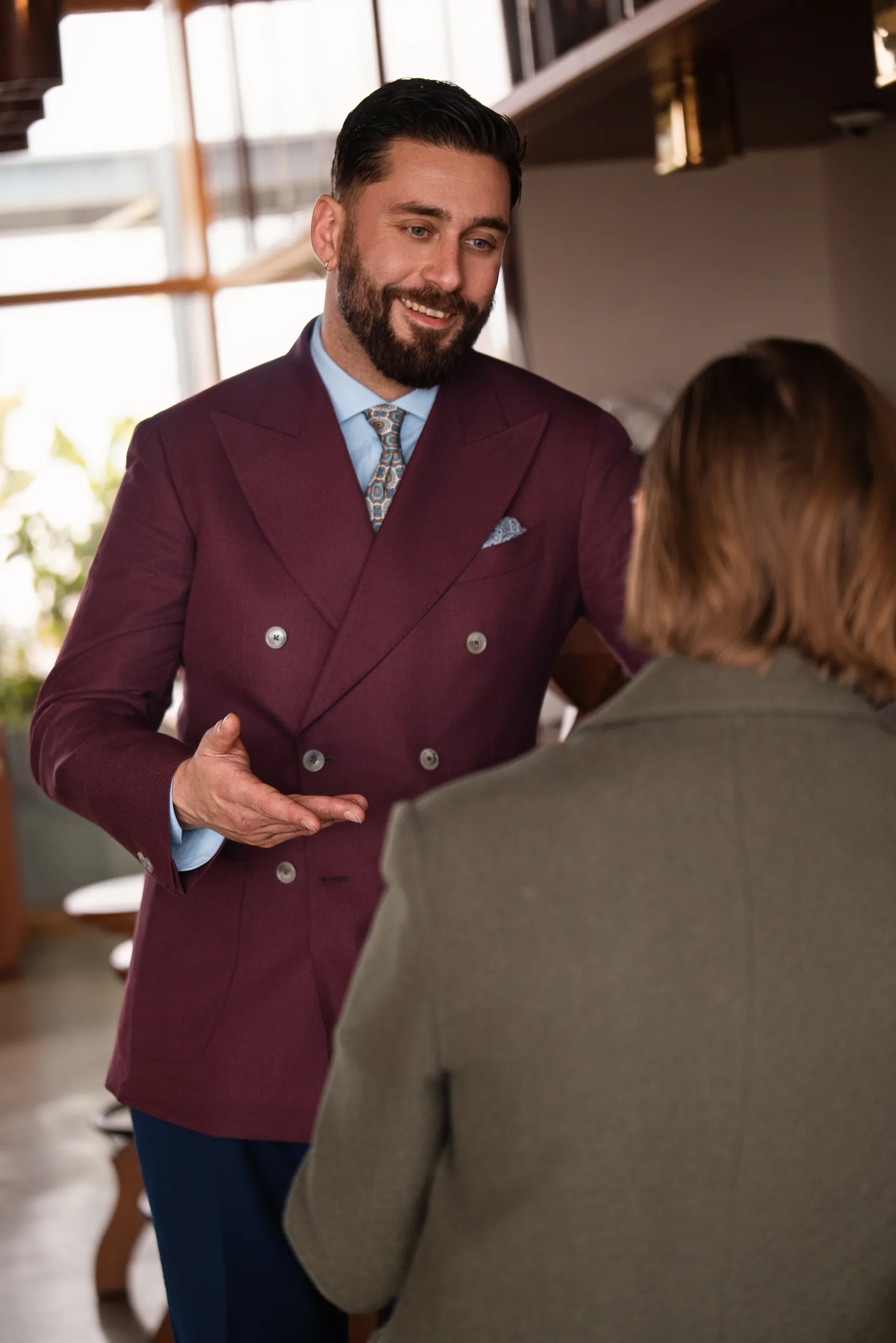 Homme en veste croisée sur mesure bordeaux en conversation dans un restaurant
