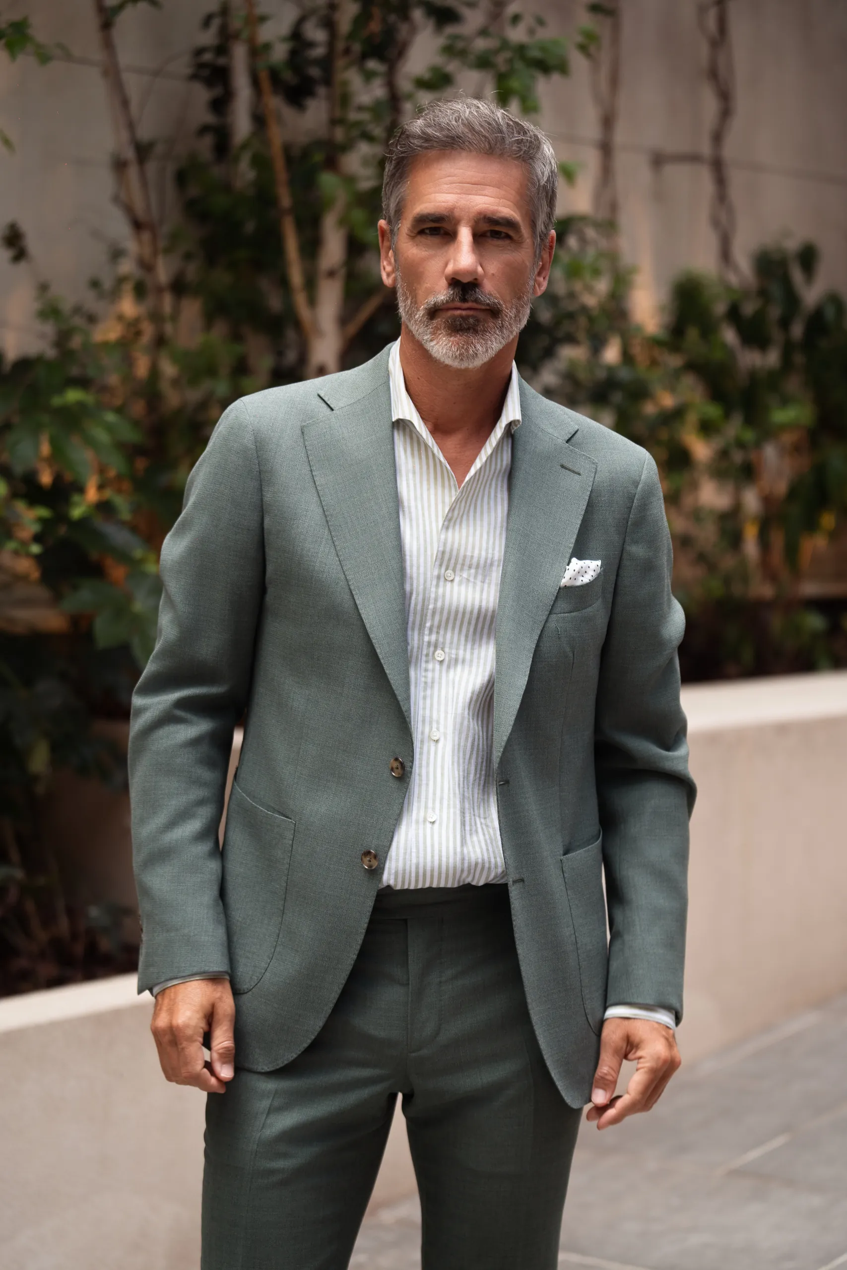 Homme en veste sur mesure vert sauge, chemise rayée et pantalon gris foncé
